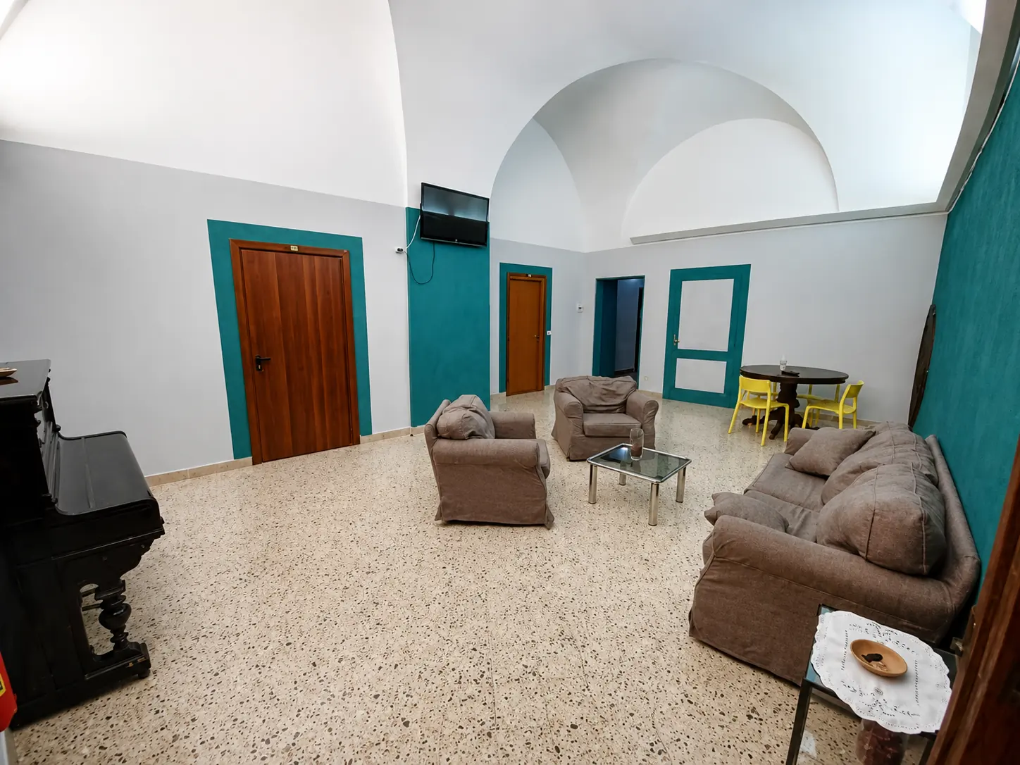 Sala comune di Domus Narnia con divani, pianoforte e pareti verde acqua